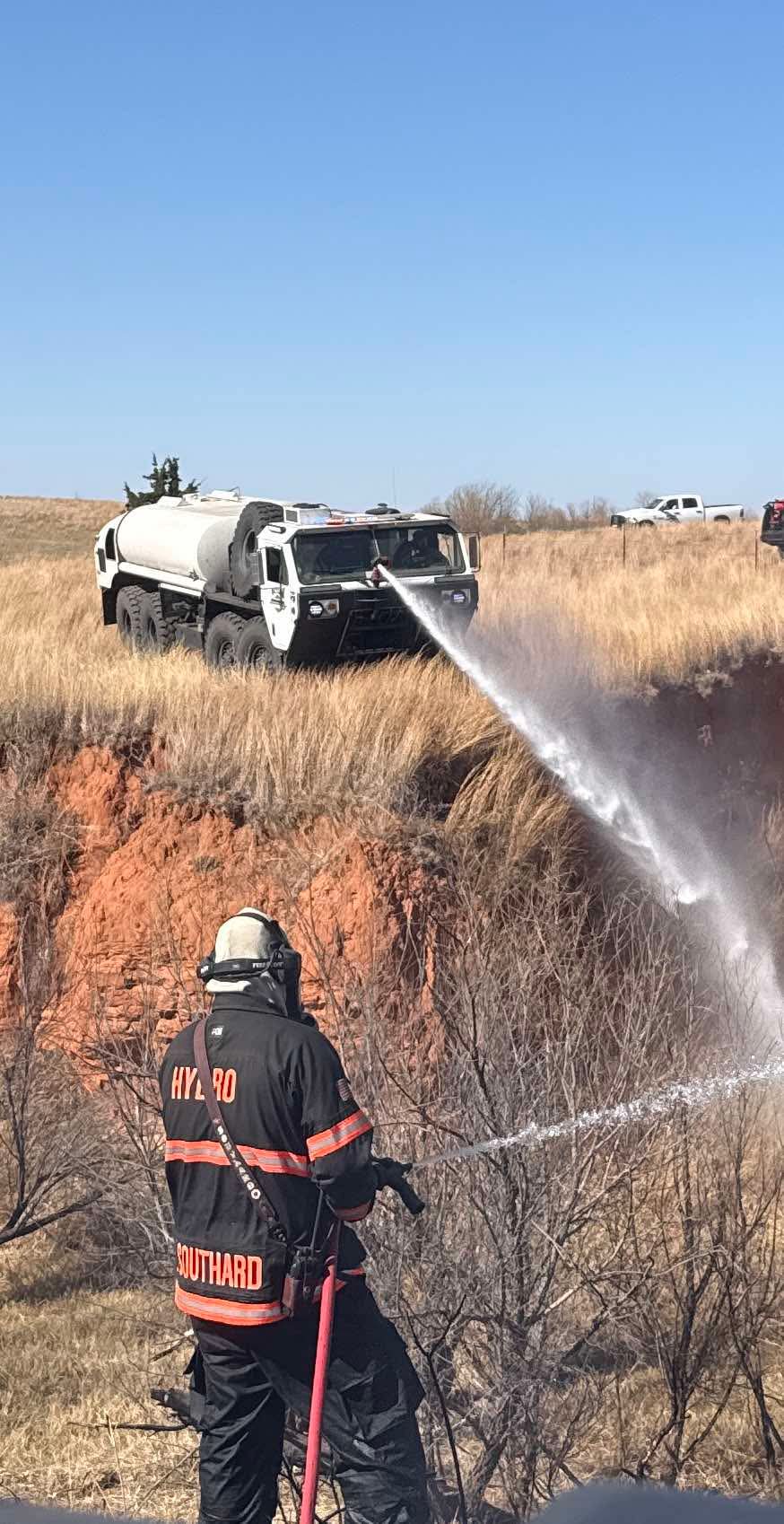 Brush truck laying down water on a grass fire