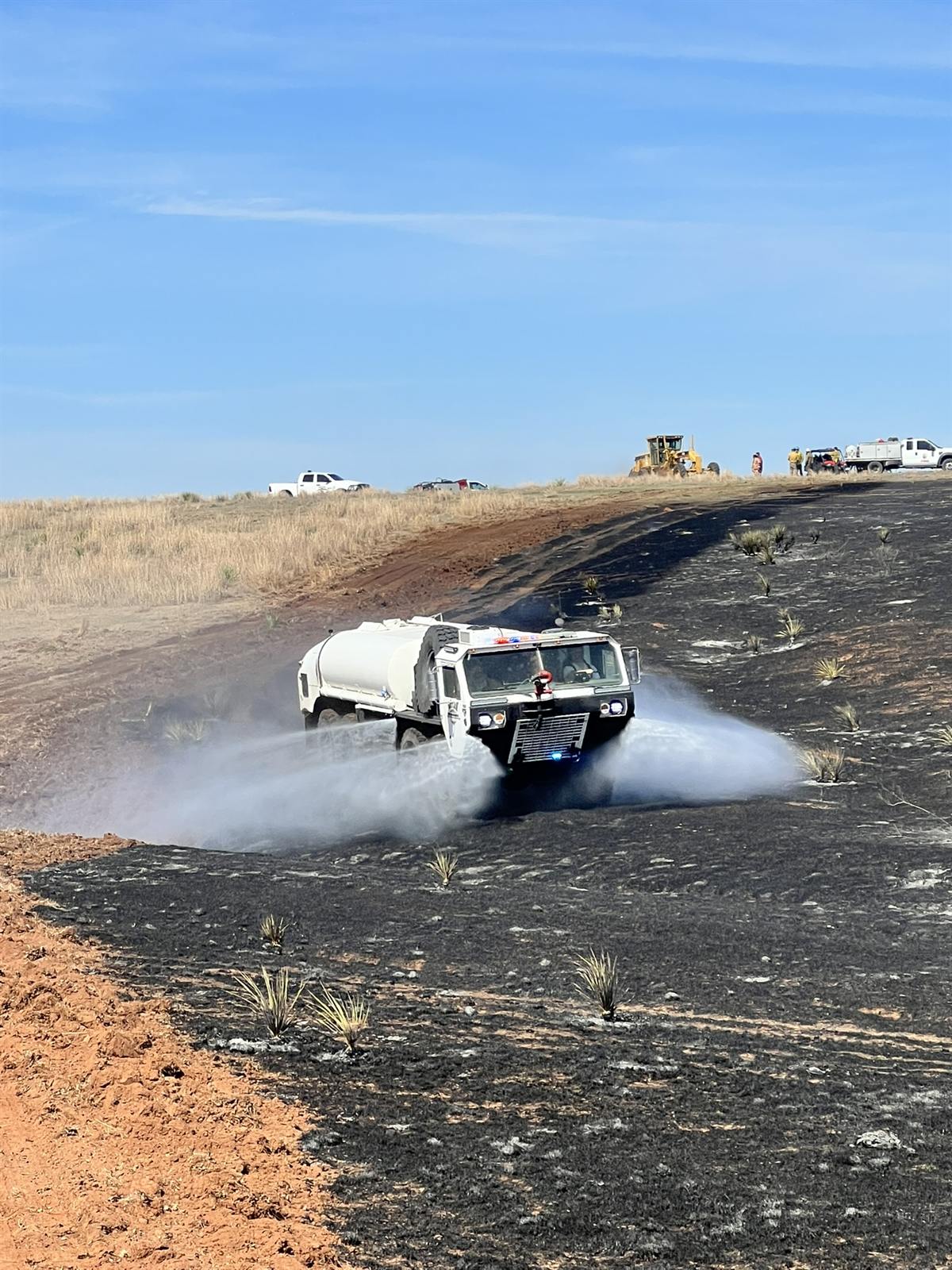 Brush truck spraying water through dust and smoke